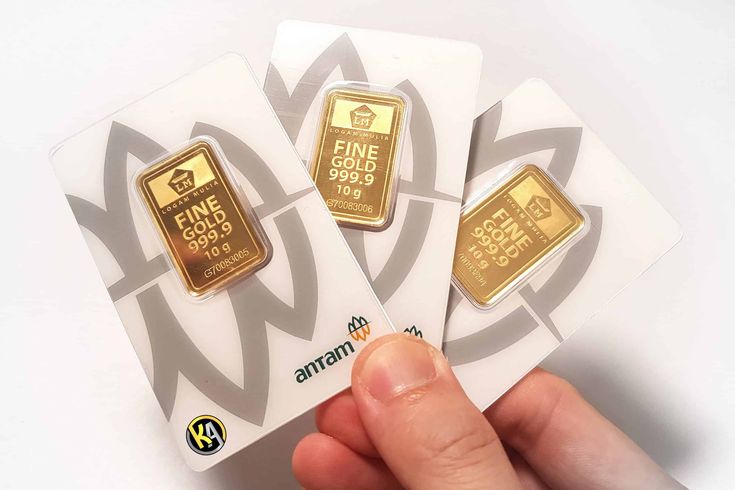 Tiga keping emas batangan Antam 10 gram bertuliskan Fine Gold 999.9 yang dipegang tangan.